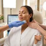 Clinician applying cool compress and performing gentle lymphatic massage to reduce swelling under a patient's chin in a modern clinic